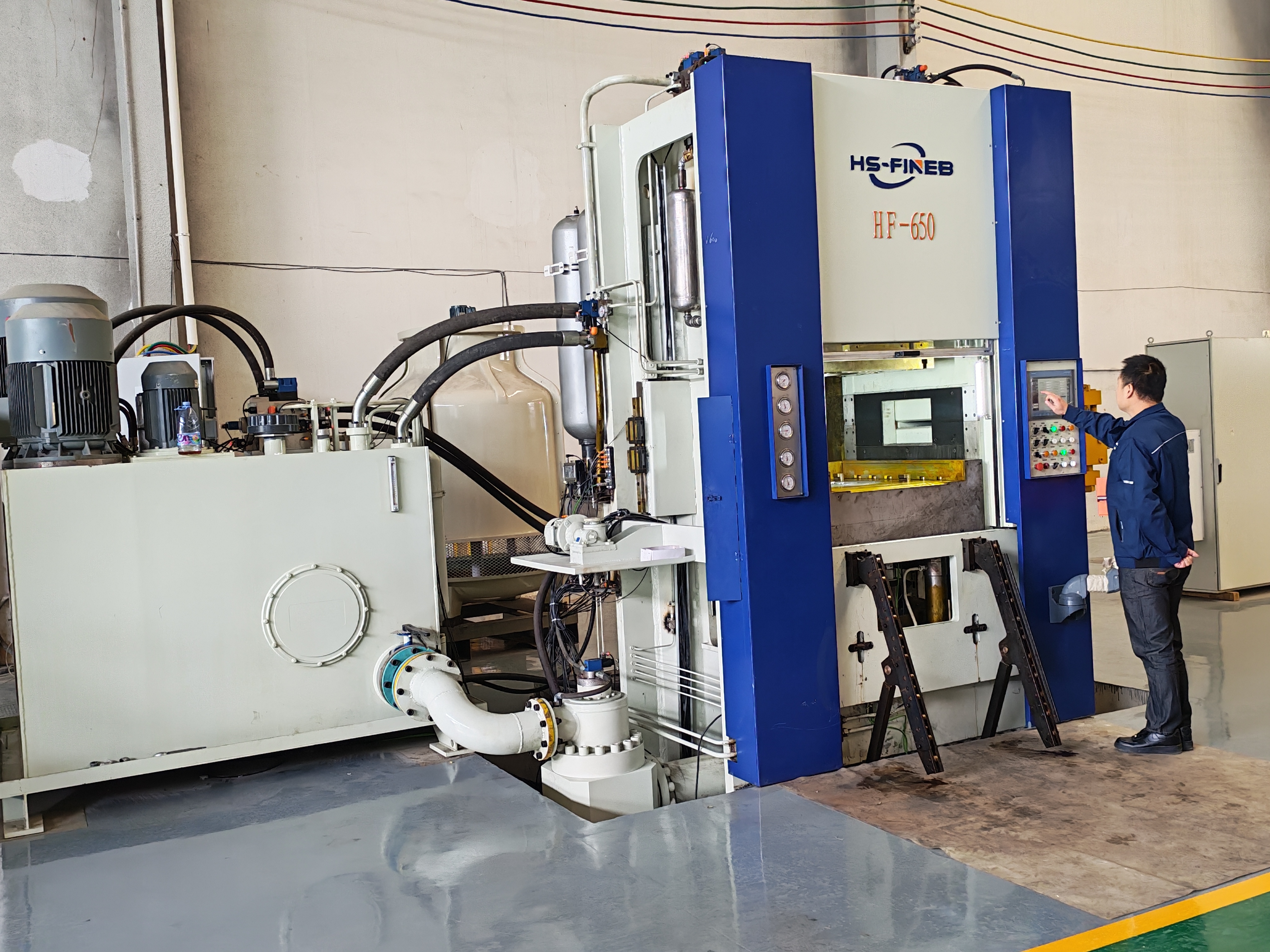 HS-FINEB technician operating HF-650 fine blanking press with hydraulic power unit in workshop